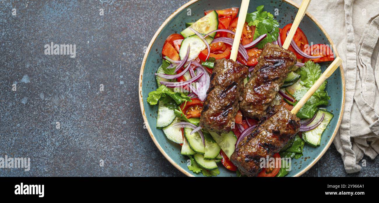 Spiedini grigliati di carne di manzo spiedini su bastoncini serviti con insalata di verdure fresche su piatto su sfondo rustico di cemento dall'alto. EAS centrale tradizionale Foto Stock