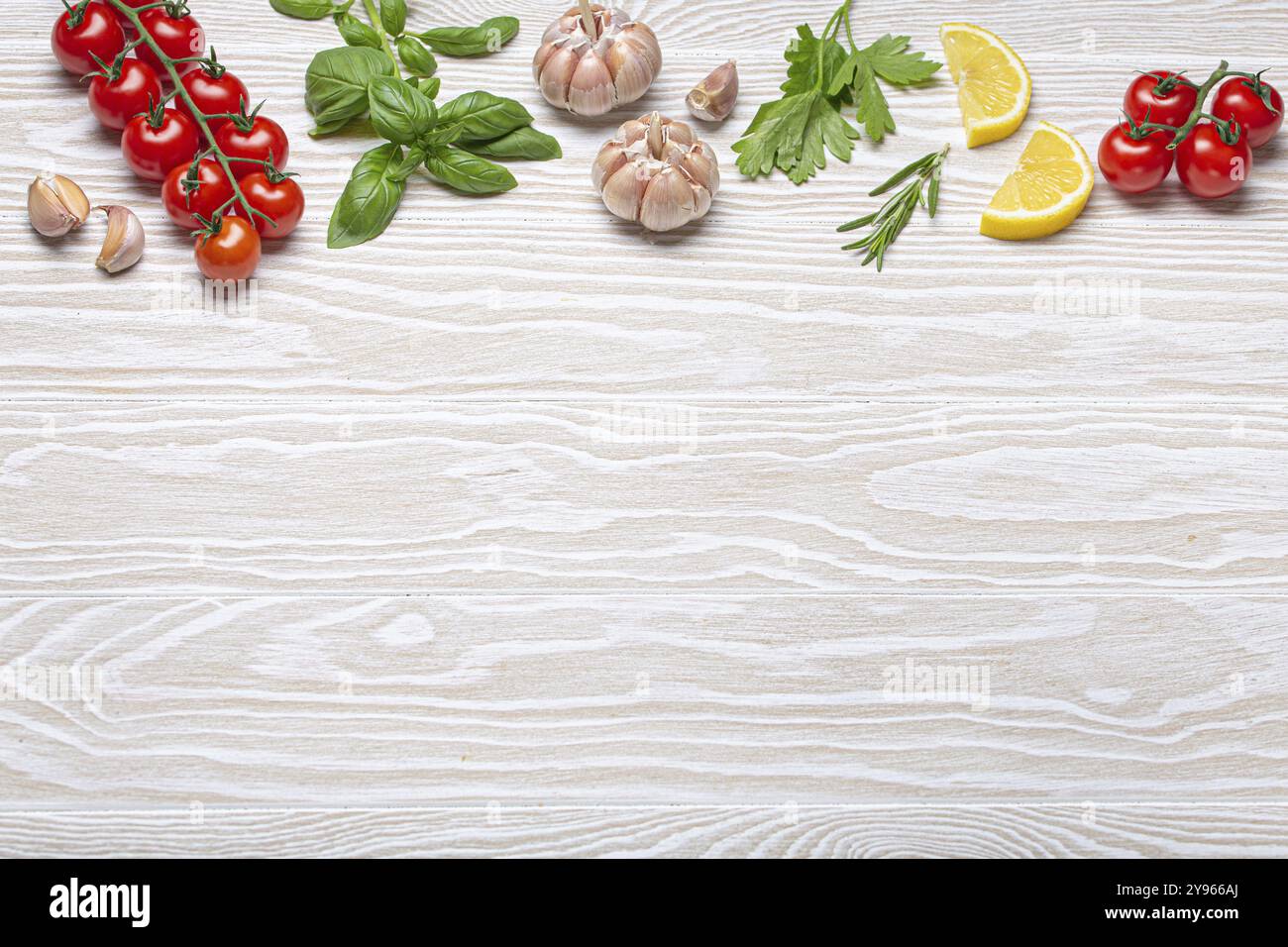 Composizione sana degli ingredienti alimentari con pomodori ciliegini freschi, erbe, spicchi d'aglio, spicchi di limone su fondo rustico in legno bianco, colpo d'aria sospeso W Foto Stock