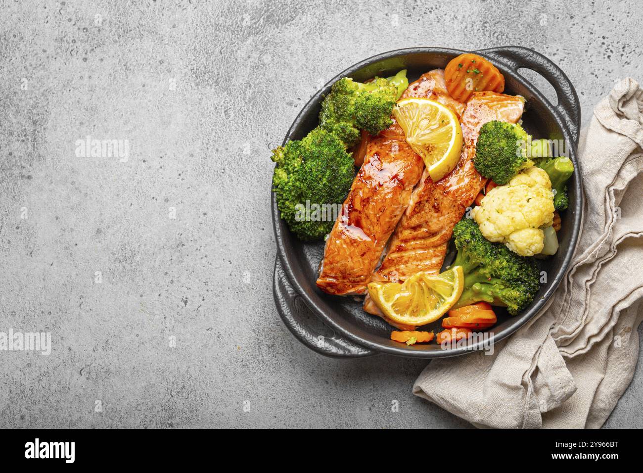 Salmone al forno, bistecche, broccoli, cavolfiore, carota in casseruola in ghisa nera su fondo in pietra grigia. Cucinare una deliziosa bassa ca Foto Stock