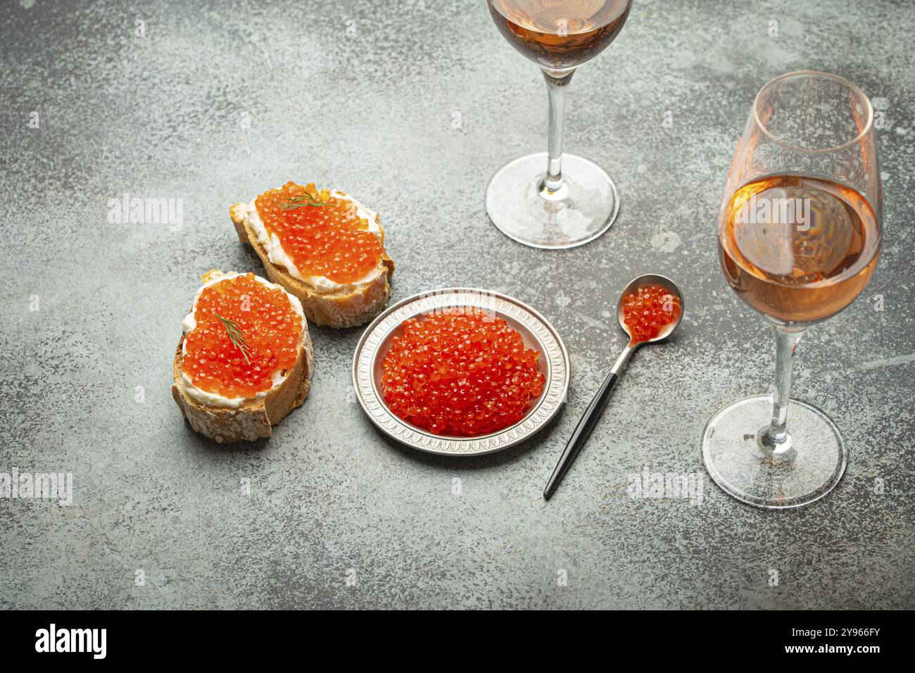 Piccolo piatto di metallo con caviale di salmone rosso, due canape al caviale, due bicchieri di champagne con vista dall'alto su sfondo grigio di cemento, un lussuoso e festoso deli Foto Stock