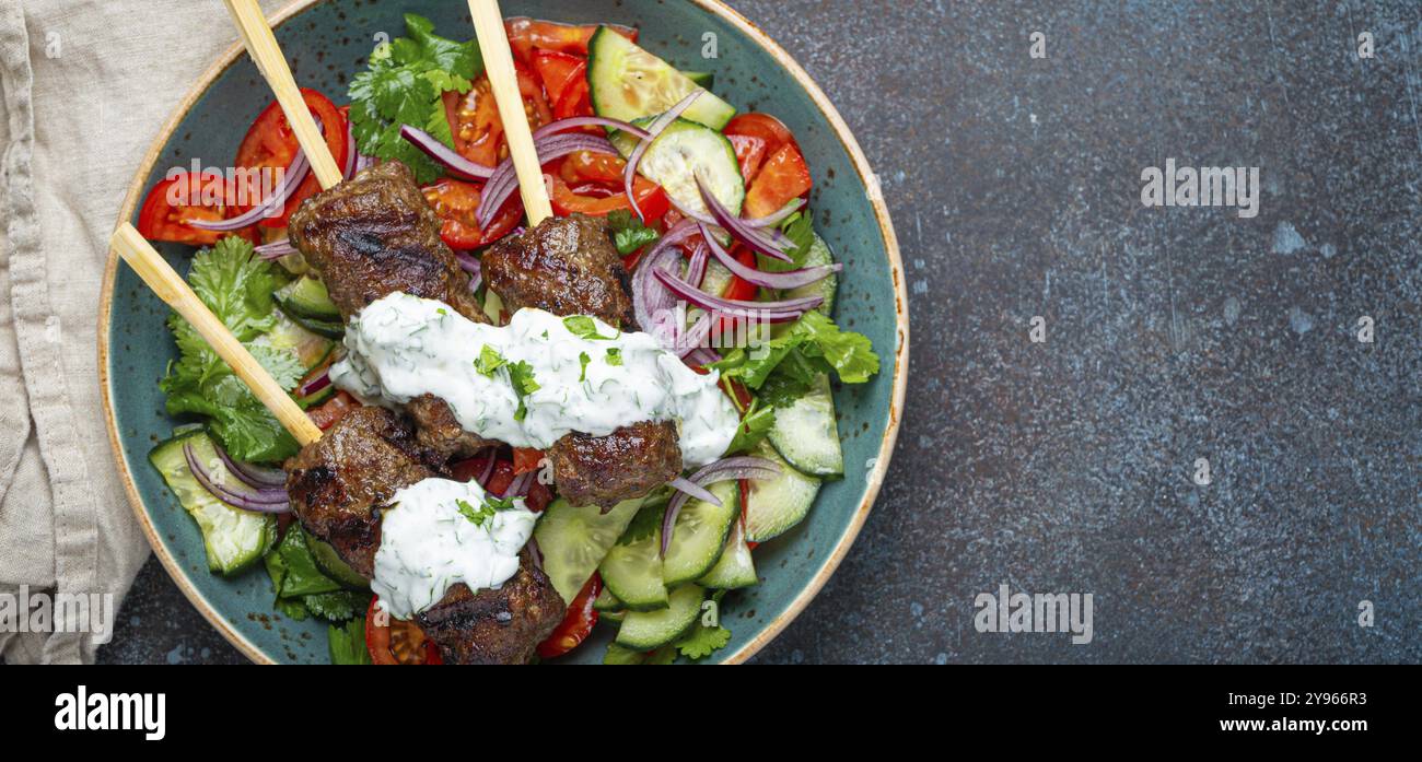 Spiedini grigliati di carne di manzo spiedini su bastoncini serviti con insalata di verdure fresche su piatto su sfondo rustico di cemento dall'alto. EAS centrale tradizionale Foto Stock
