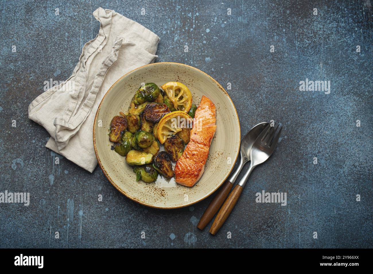 Delizioso filetto di salmone con germogli di Bruxelles grigliati sul piatto, vista dall'alto su sfondo rustico in pietra. Cena salutare con pesce alla griglia e verdure, Bal Foto Stock