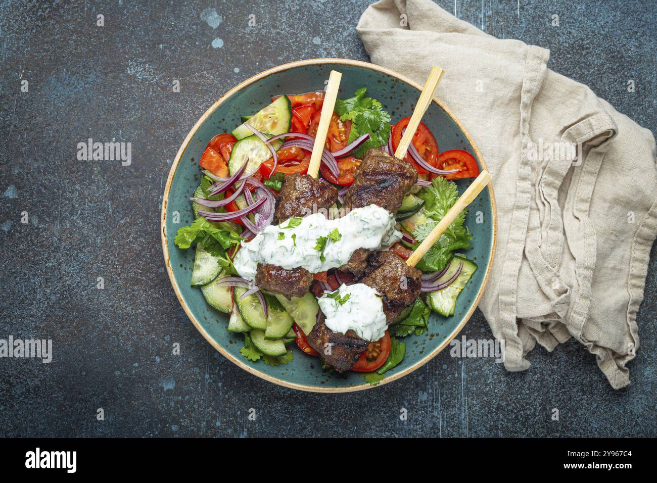 Spiedini grigliati di carne di manzo spiedini su bastoncini serviti con insalata di verdure fresche su piatto su sfondo rustico di cemento dall'alto. EAS centrale tradizionale Foto Stock