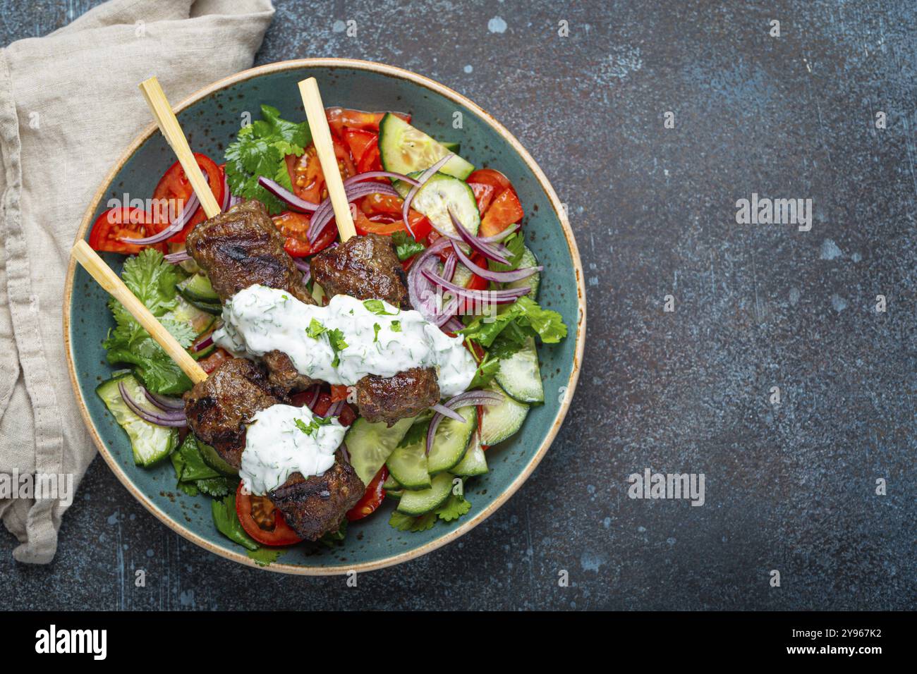 Spiedini grigliati di carne di manzo spiedini su bastoncini serviti con insalata di verdure fresche su piatto su sfondo rustico di cemento dall'alto. EAS centrale tradizionale Foto Stock