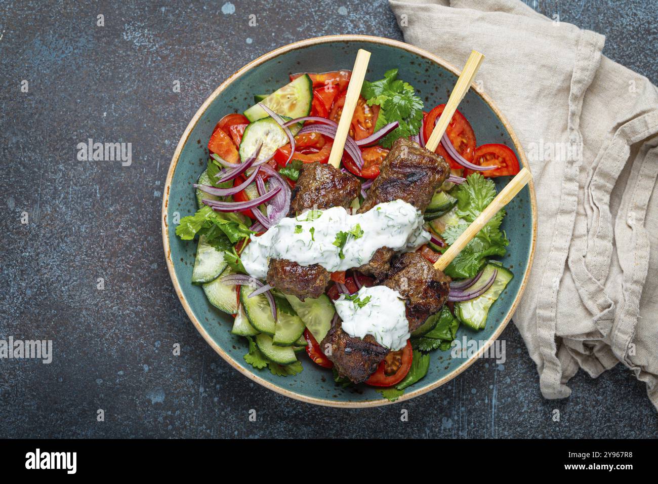 Spiedini grigliati di carne di manzo spiedini su bastoncini serviti con insalata di verdure fresche su piatto su sfondo rustico di cemento dall'alto. EAS centrale tradizionale Foto Stock