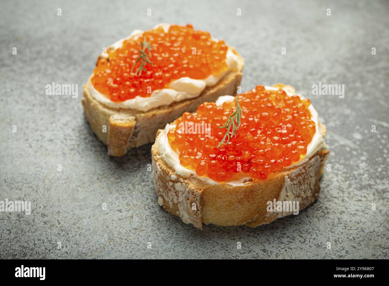 Due crostini di caviale baguette con burro e caviale di salmone rosso, vista dall'alto su sfondo grigio di cemento, prelibatezze e antipasti di lusso, cibo Foto Stock