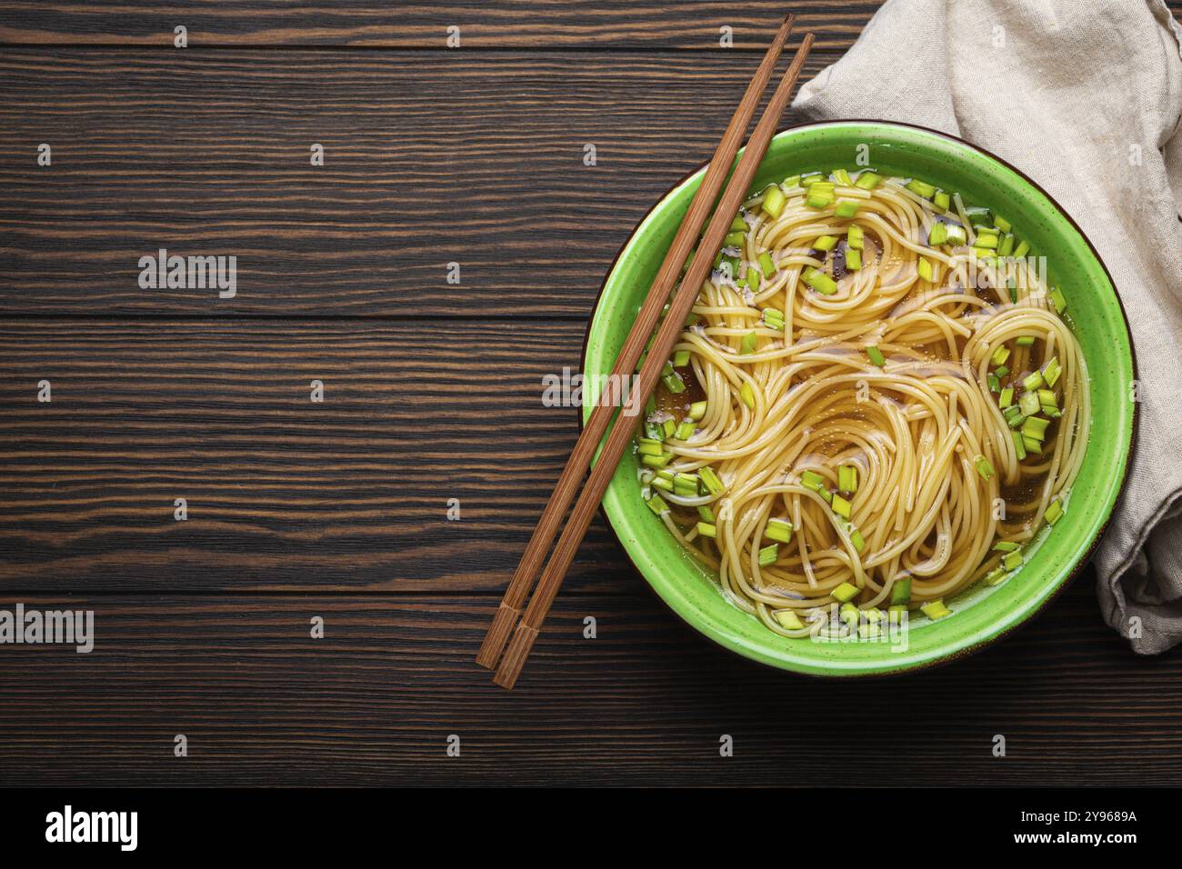 Zuppa di noodles asiatici in una ciotola in ceramica rustica verde con bacchette di legno vista dall'alto su sfondo di legno scuro. Spaghetti di mein lo con bouillon e oni verdi Foto Stock