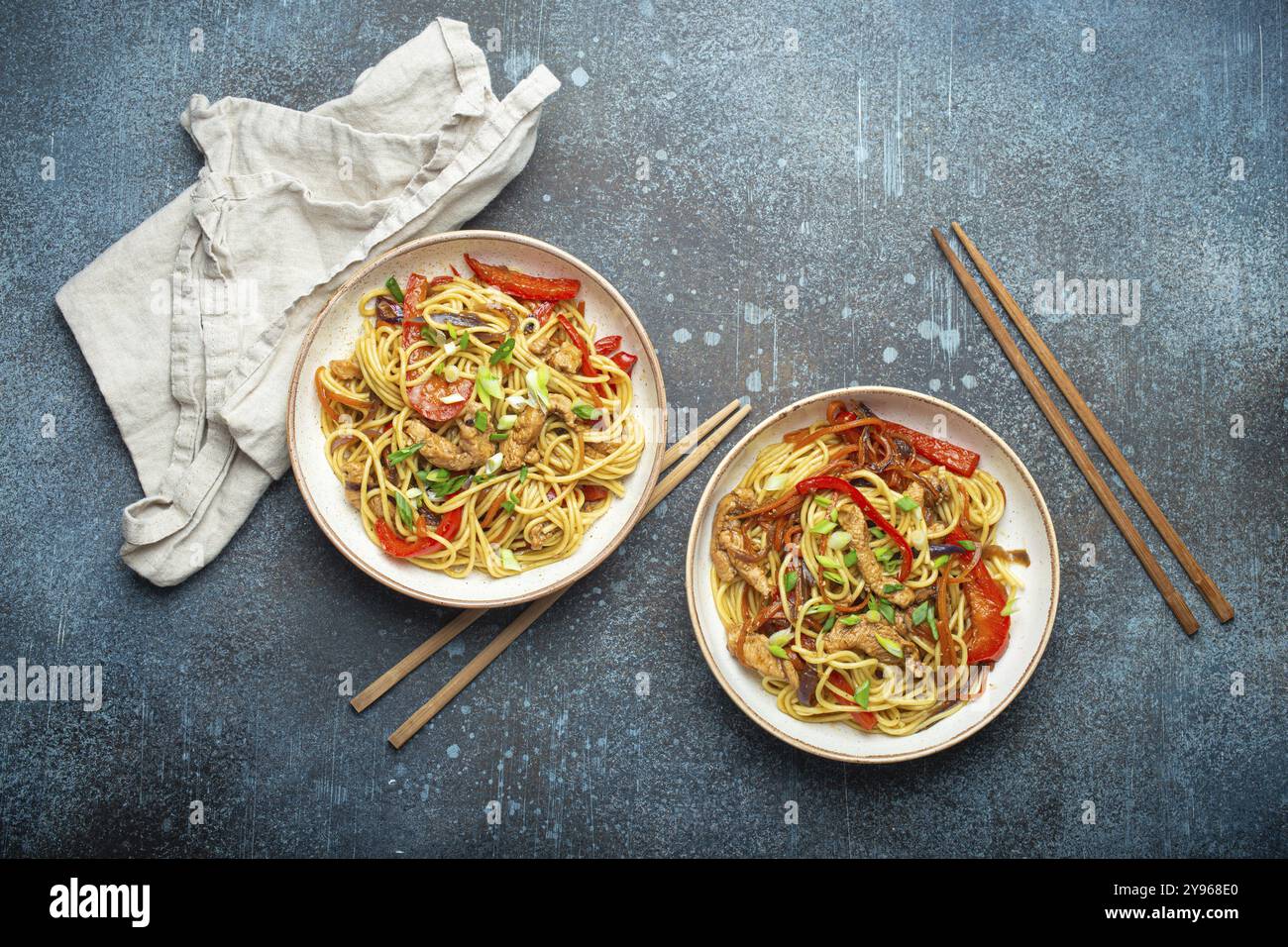 Due ciotole con Chow Mein o lo Mein, tradizionali spaghetti cinesi con carne e verdure, serviti con bacchette e vista dall'alto su rustico blu Foto Stock