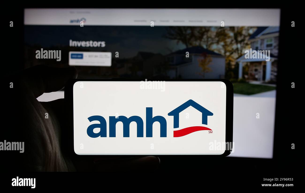 Persona che detiene un cellulare con il logo della società americana American Homes 4 Rent LP (AMH) sullo schermo di fronte alla pagina Web aziendale. Mettere a fuoco il display del telefono. Foto Stock