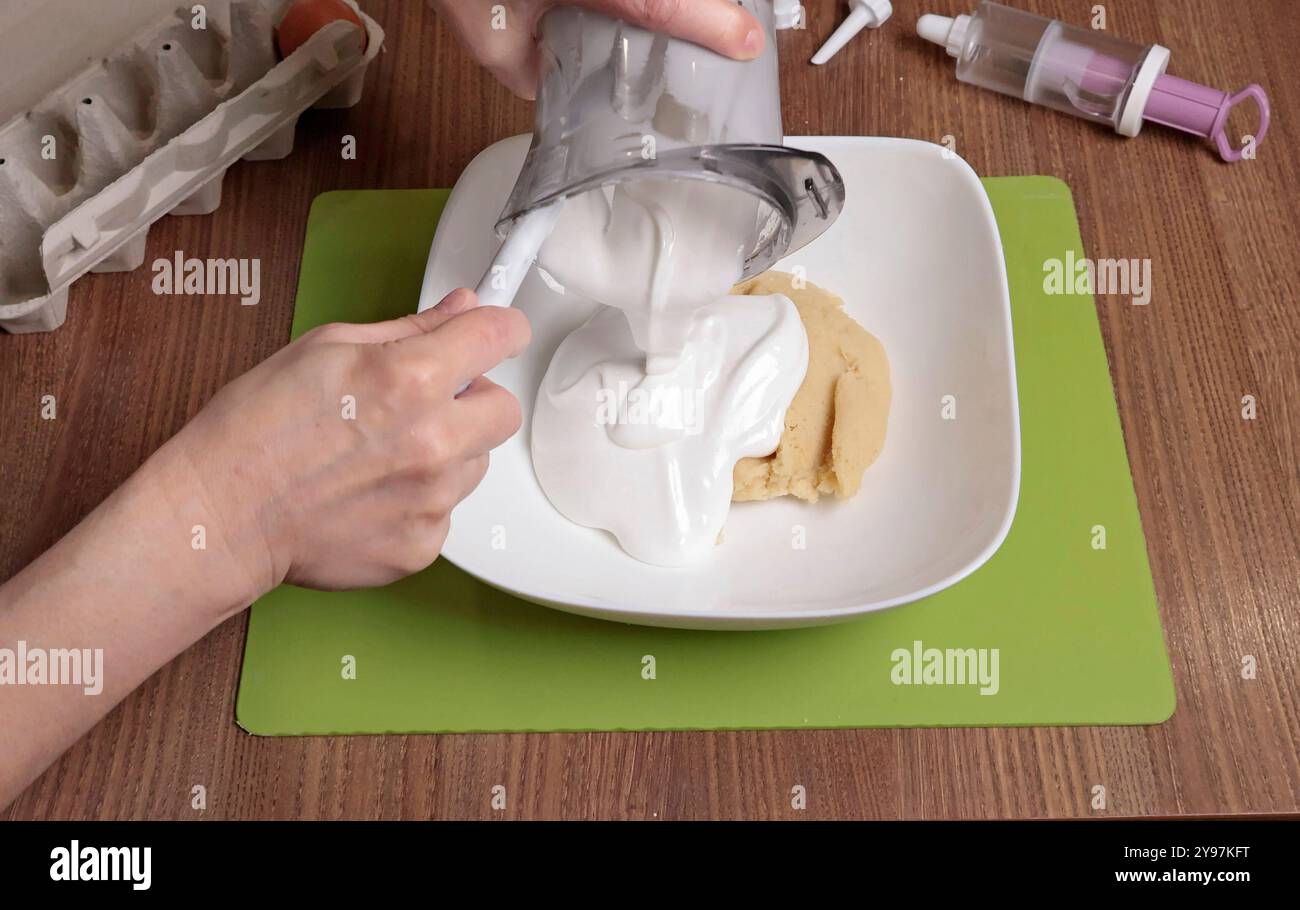 Processo di preparazione dell'impasto. Donna mescolare nel recipiente lo zucchero a velo, la farina di mandorle e l'albume sbattuto con una spatola al silicone. Preparare i macaron a casa. Chiudi Foto Stock