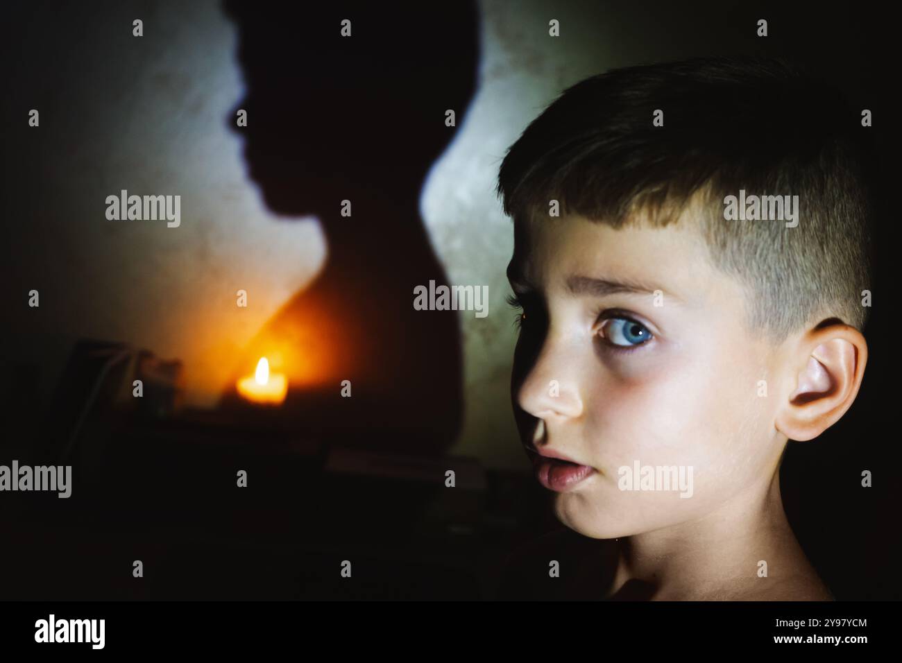 Guerra e blackout in Ucraina. Ritratto di un adolescente in un appartamento cittadino durante un blackout. Candele accese e lanterna a LED illuminano la stanza. Foto Stock