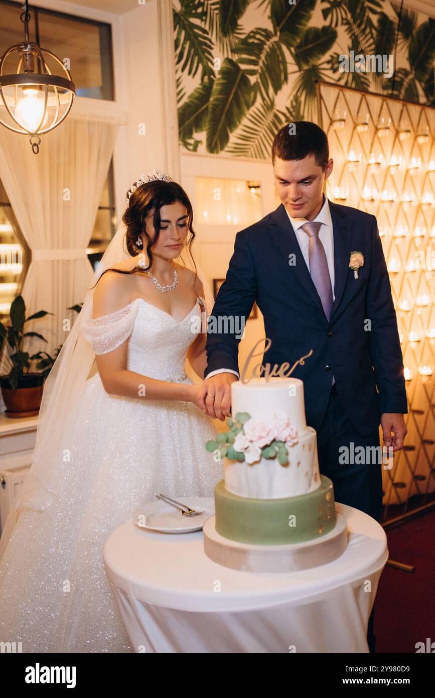 gli sposi novelli tagliano felicemente, ridono e assaggiano la torta di nozze Foto Stock