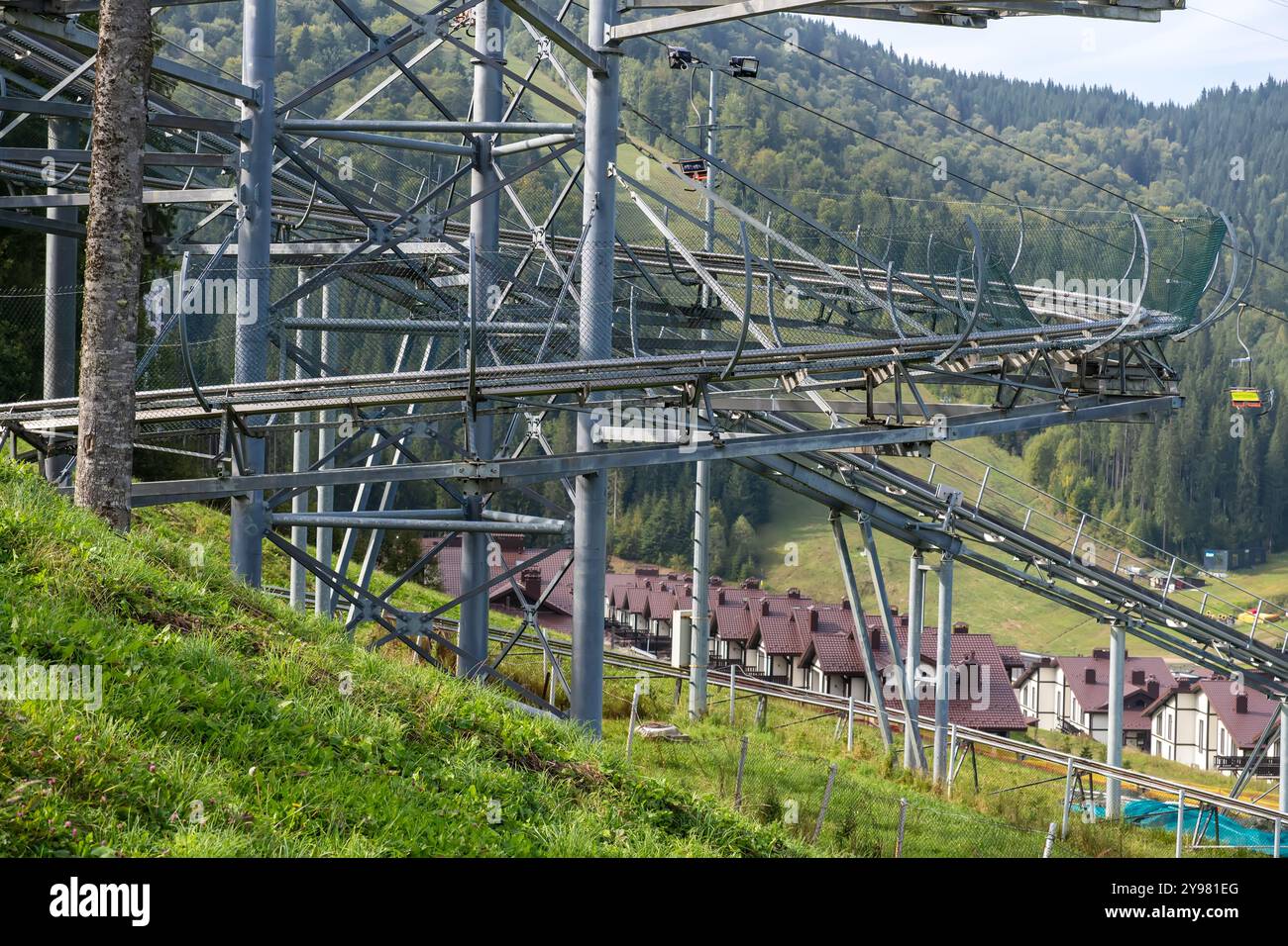 Una pista estiva di slittino con molte curve nel mezzo di una foresta di montagna con vista sugli impianti di risalita. Un'attrazione per una discesa emozionante con Foto Stock