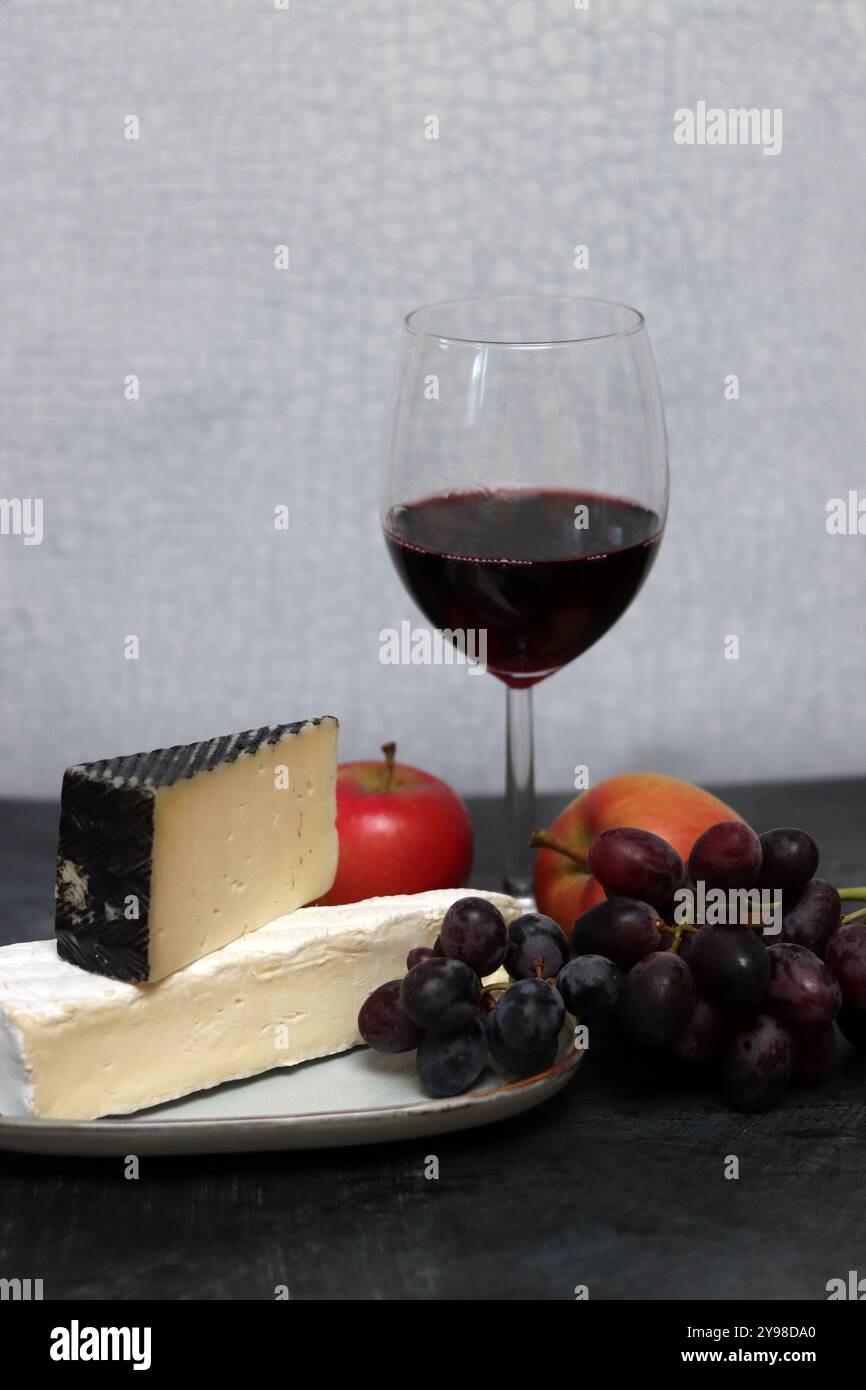 Vassoio di formaggi con uva, vino rosso e mela su sfondo grigio Foto Stock