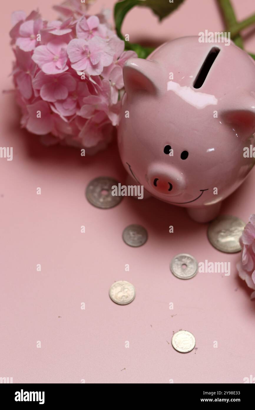 Salvadanaio rosa con monete e ortensie su sfondo rosa con spazio per il testo. Concetto di alfabetizzazione finanziaria. Foto Stock