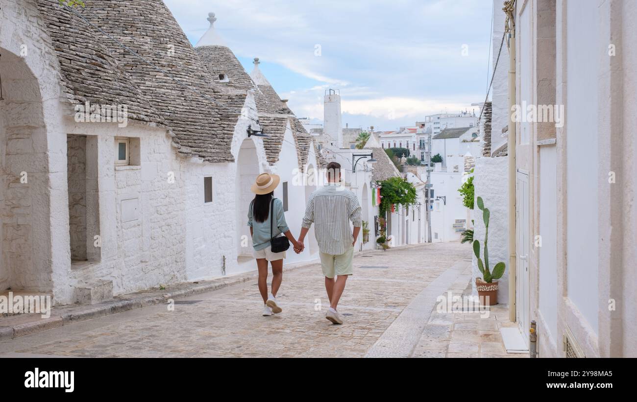 Un paio cammina mano nella mano lungo una stretta strada acciottolata fiancheggiata da case di trulli imbiancate, immergendosi nella bellezza dell'uniq di Alberobello Puglia Foto Stock