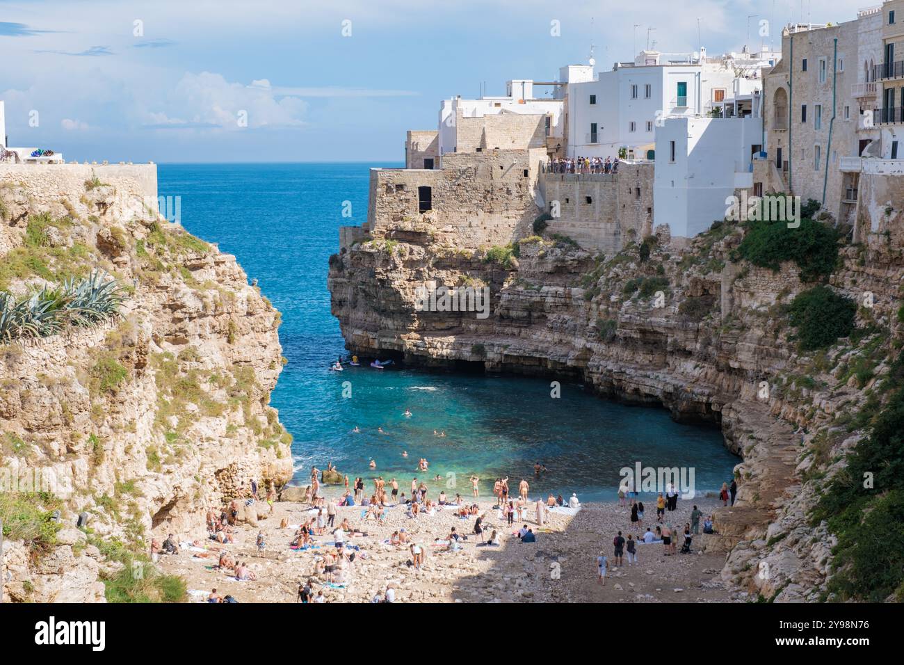 I visitatori di Polignano a Mare si divertono nella baia nascosta della Puglia sotto il sole italiano, godendosi le acque cristalline tra le scogliere storiche e l'affascinante whitewa Foto Stock