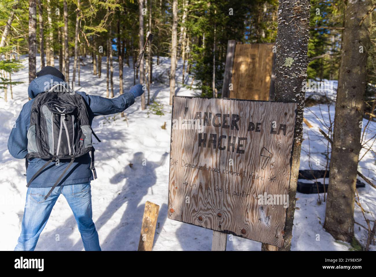 L'escursionista sta lanciando un'ascia a un bersaglio di legno in una foresta innevata, godendosi le attività invernali all'aperto. Messa a fuoco selettiva Foto Stock