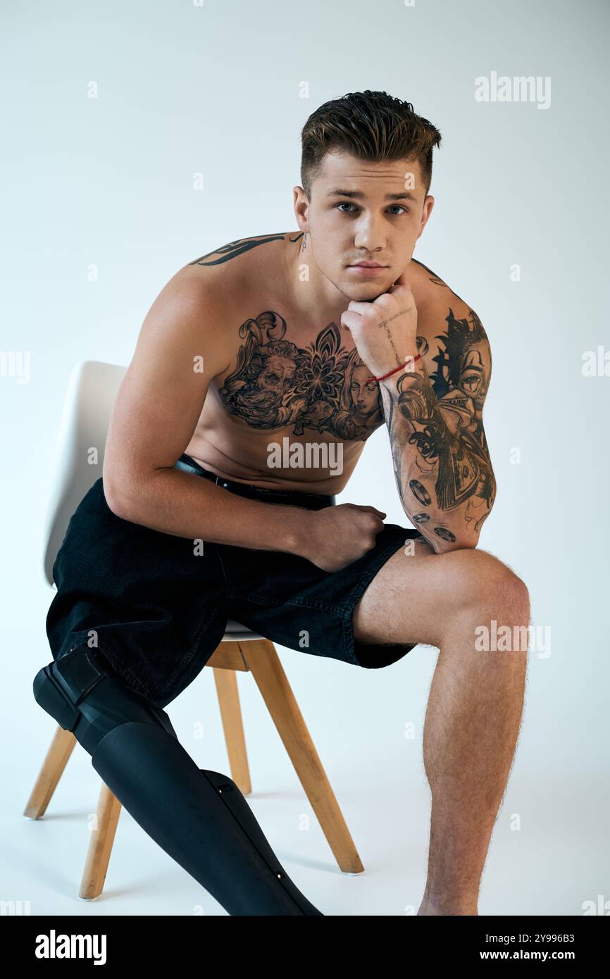 Un giovane tatuato siede con cura su una sedia, mostrando la sua gamba protesica e la sua complessa arte del corpo. Foto Stock