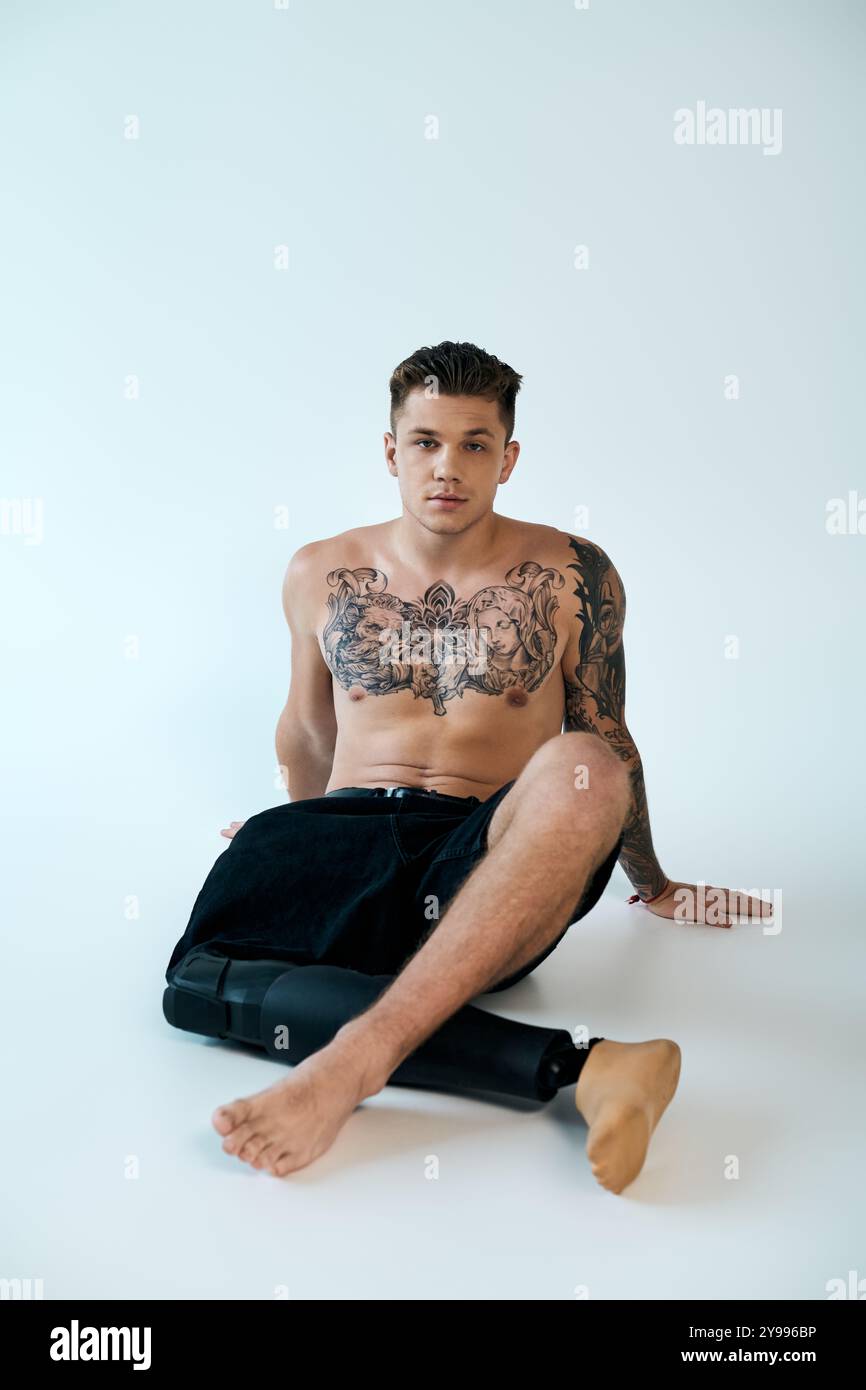 Un giovane con tatuaggi intricati mostra la sua gamba protesica mentre è seduto in un luminoso studio. Foto Stock