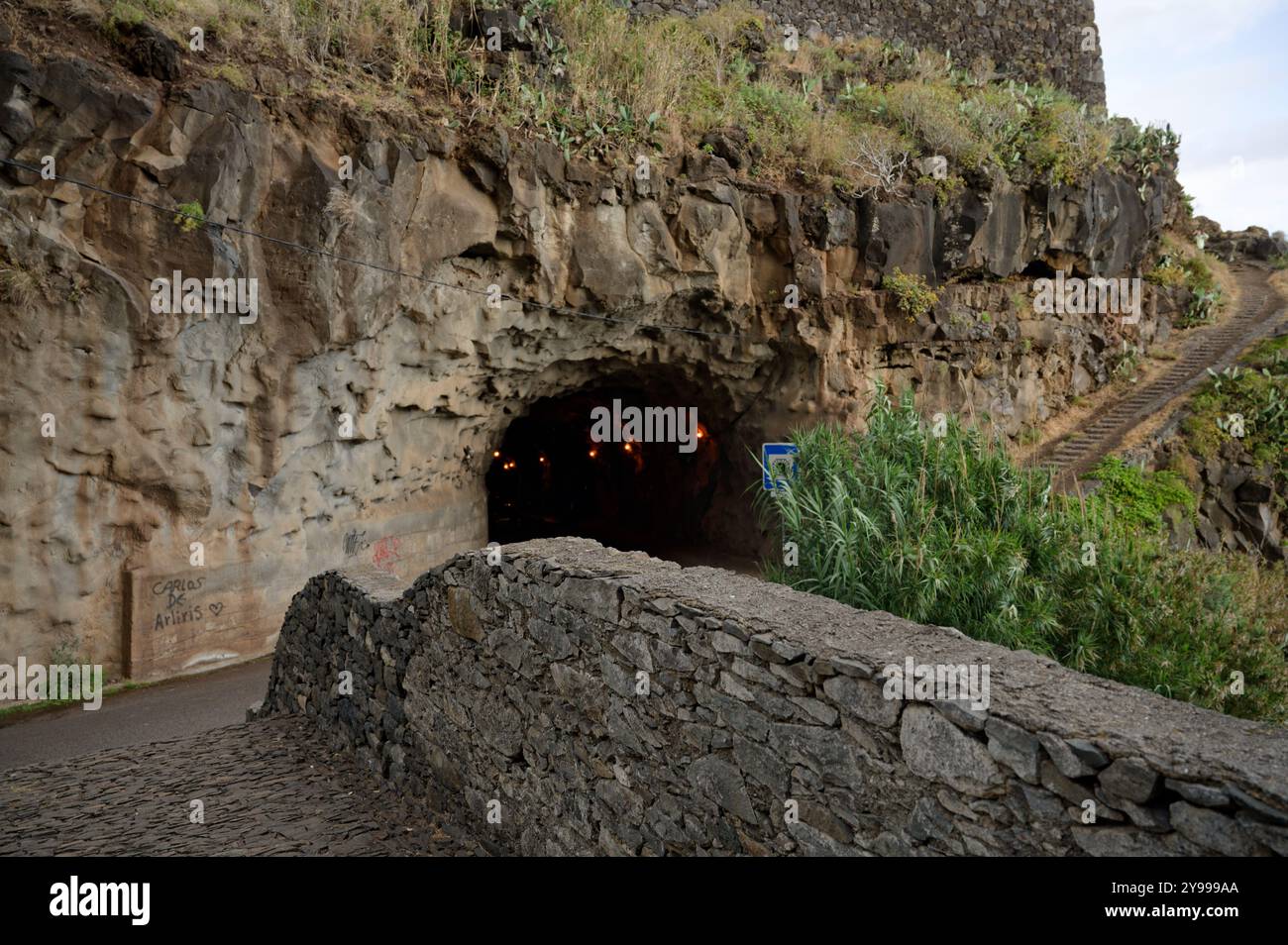 Tunnel roccioso scavato attraverso le scogliere di Madeira, con un ponte di ciottoli e un sentiero collinare Foto Stock