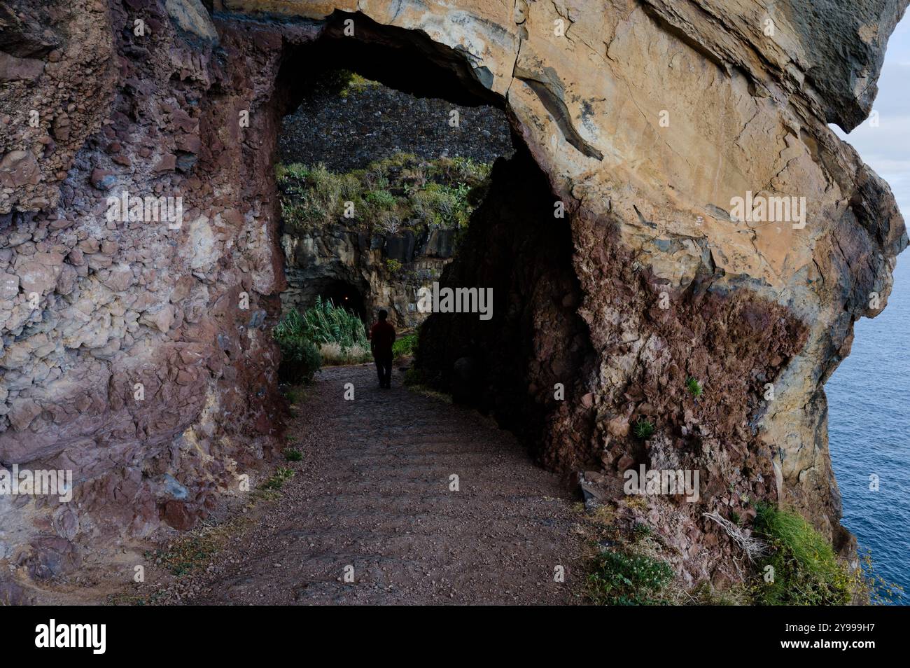 La figura solitaria attraversa un tunnel naturale scavato nelle scogliere lungo la costa di Madeira Foto Stock