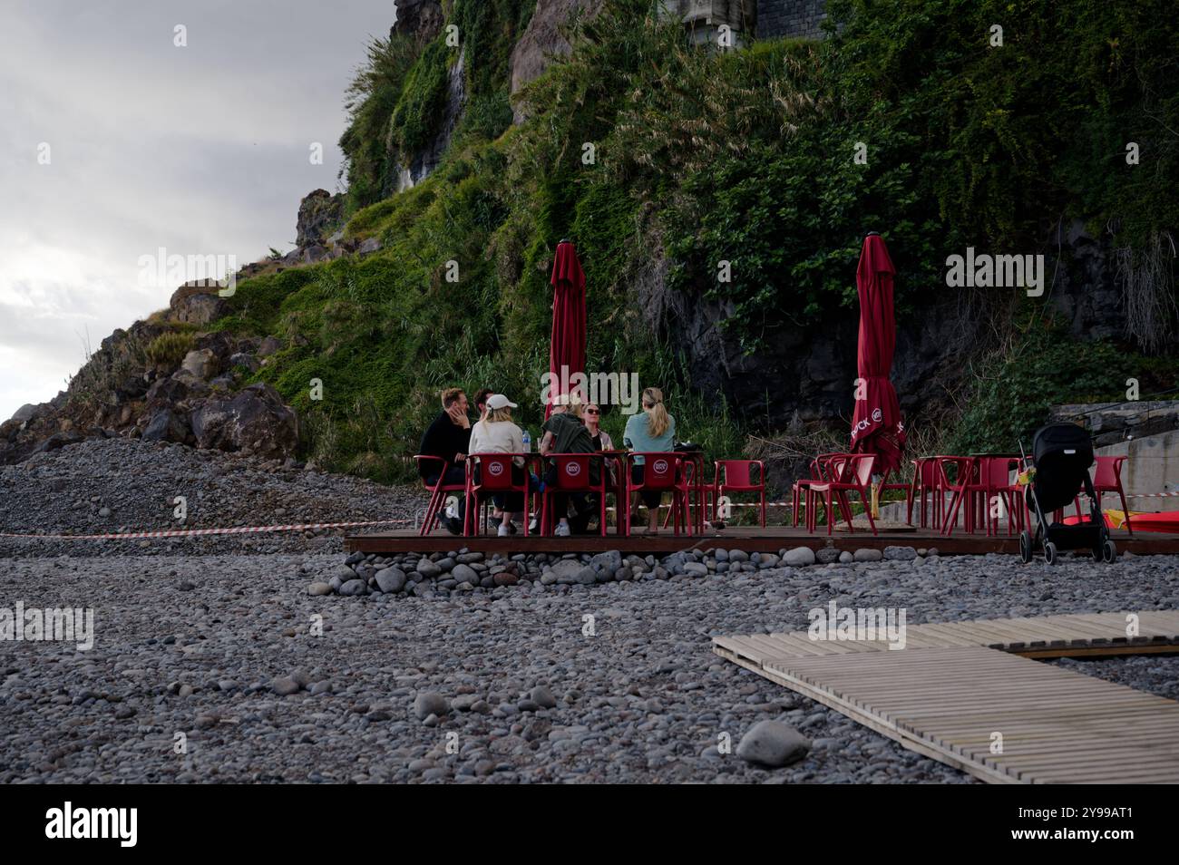 Amici che si godono una caffetteria sul mare su una costa rocciosa sotto le scogliere ricoperte di vegetazione Foto Stock