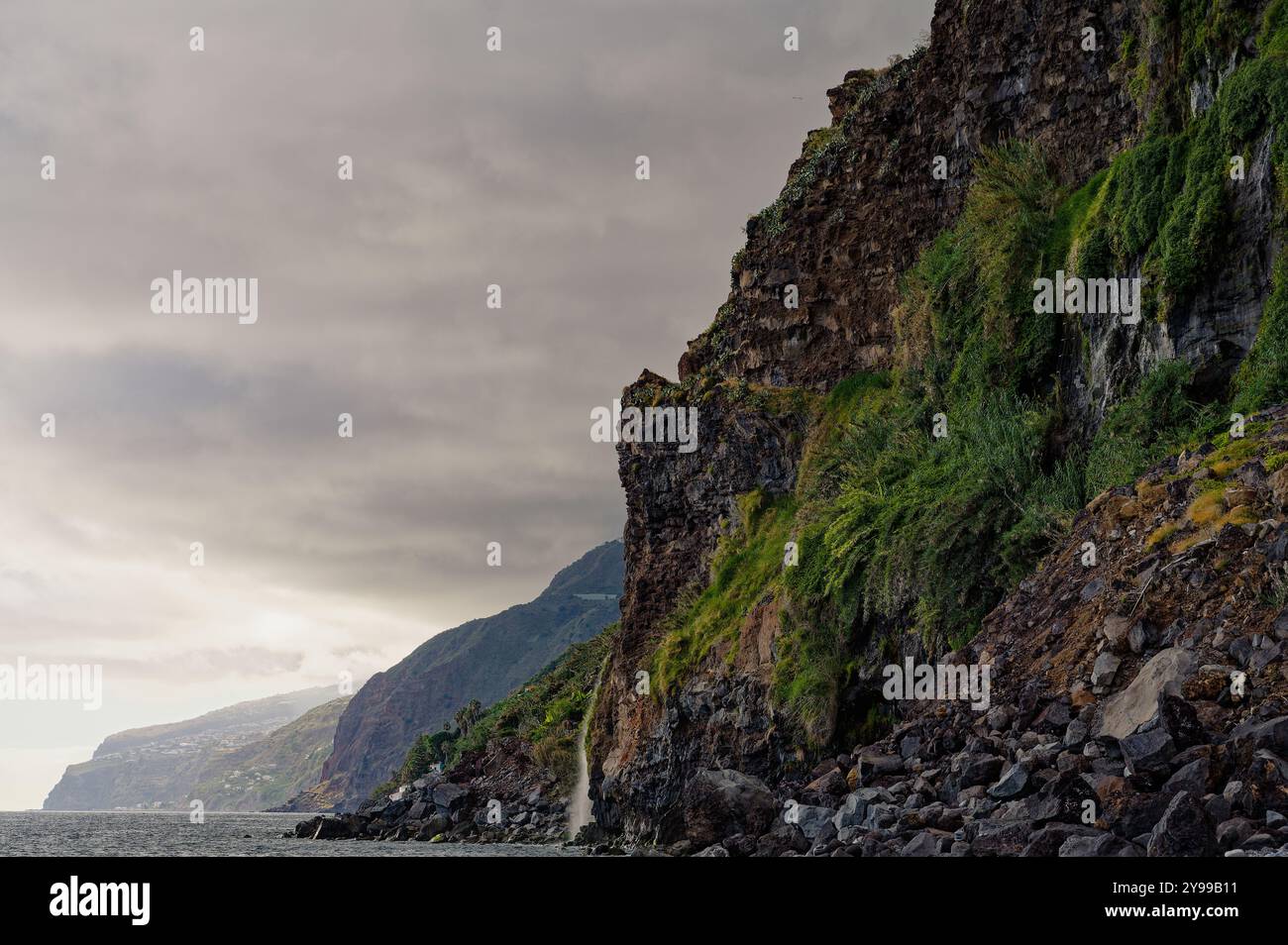 Scogliere aspre con vegetazione lussureggiante si estendono lungo la spettacolare costa di madeira sotto cieli molli Foto Stock