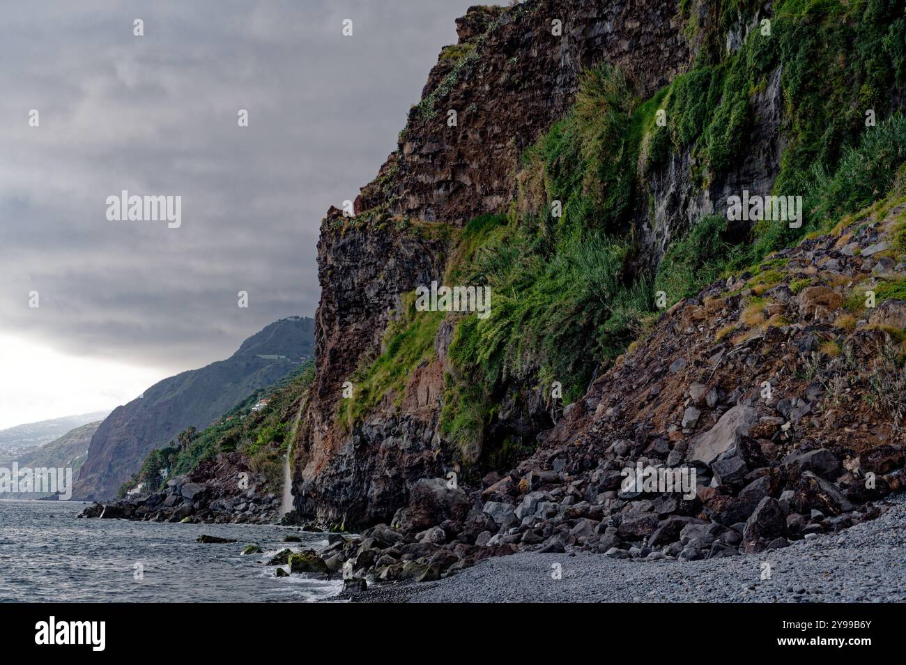 Scogliere aspre con vegetazione lussureggiante si estendono lungo la spettacolare costa di madeira sotto cieli molli Foto Stock