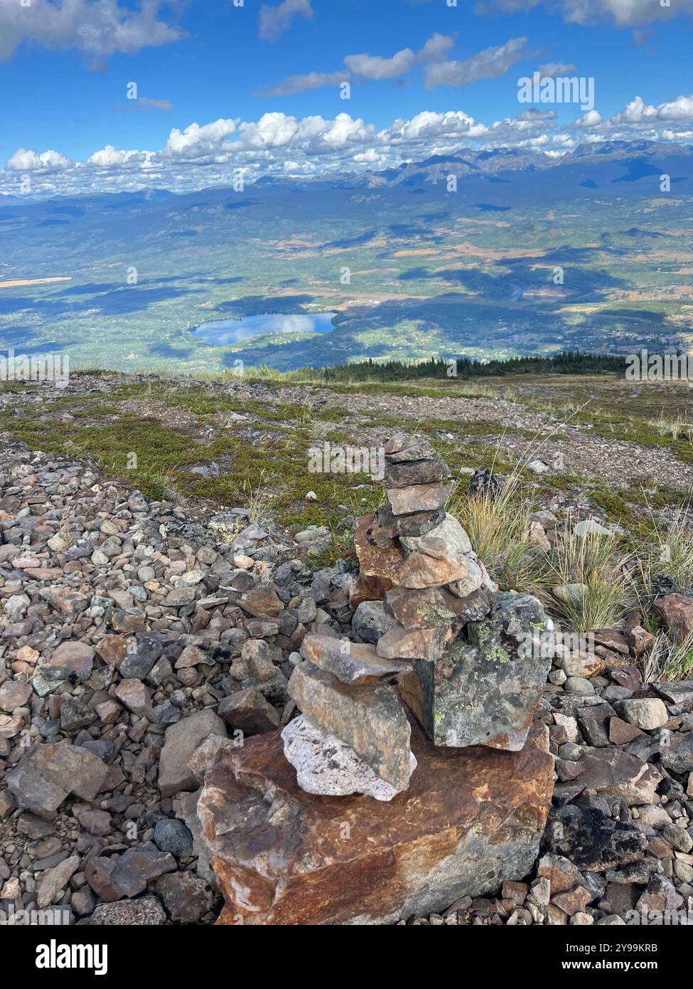 Vista panoramica dal sentiero Round the Mountain sulla Hudson Bay Mountain, affacciato su Smithers, British Columbia, con pietre di cairn, ampia valle, e catene montuose - Immagine stock catturata con smartphone
