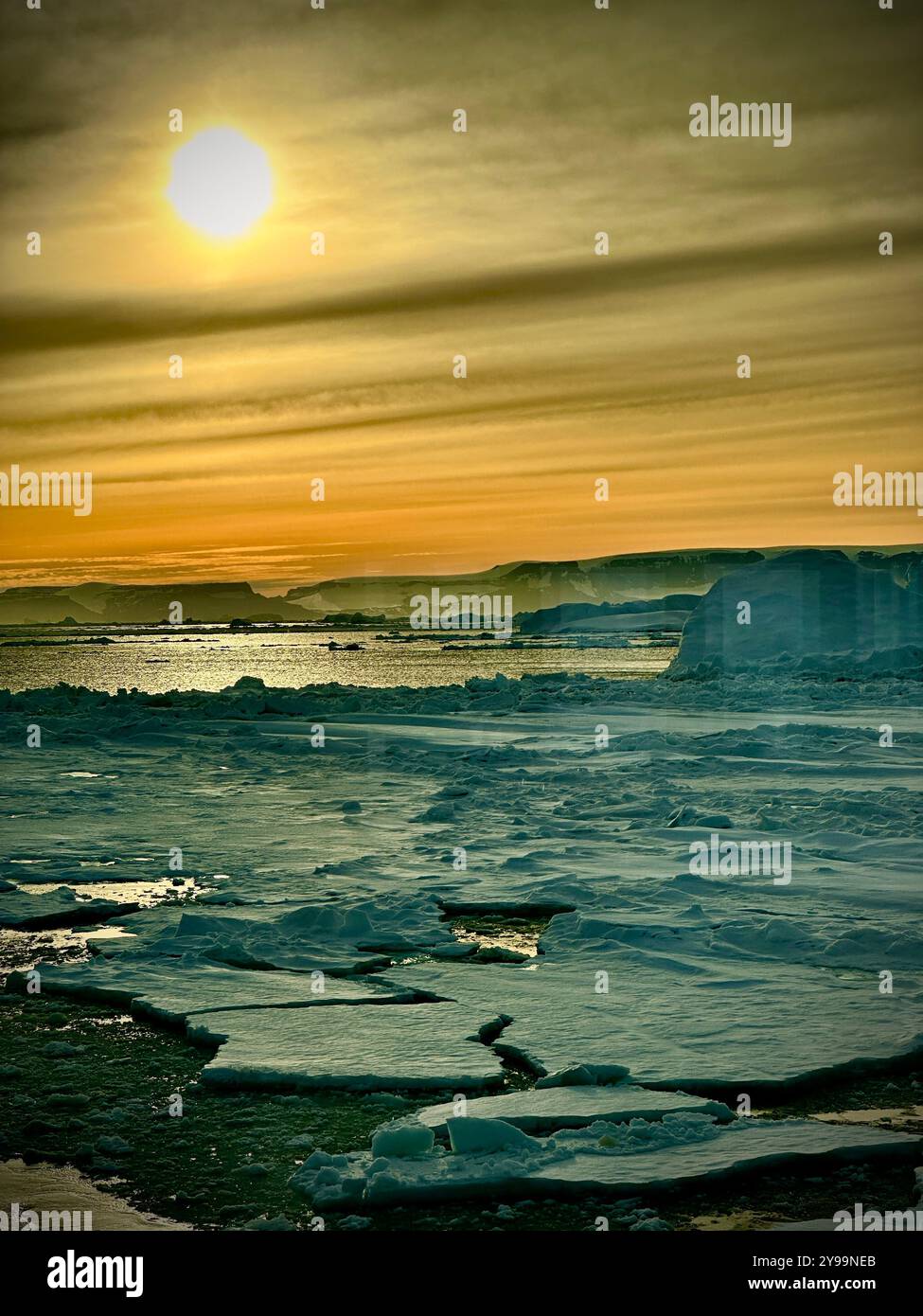 Il sole del solstizio d'inverno crea un bagliore dorato mozzafiato sul ghiacciato Oceano meridionale in Antartide, evidenziando il paesaggio ghiacciato e sereno Foto Stock