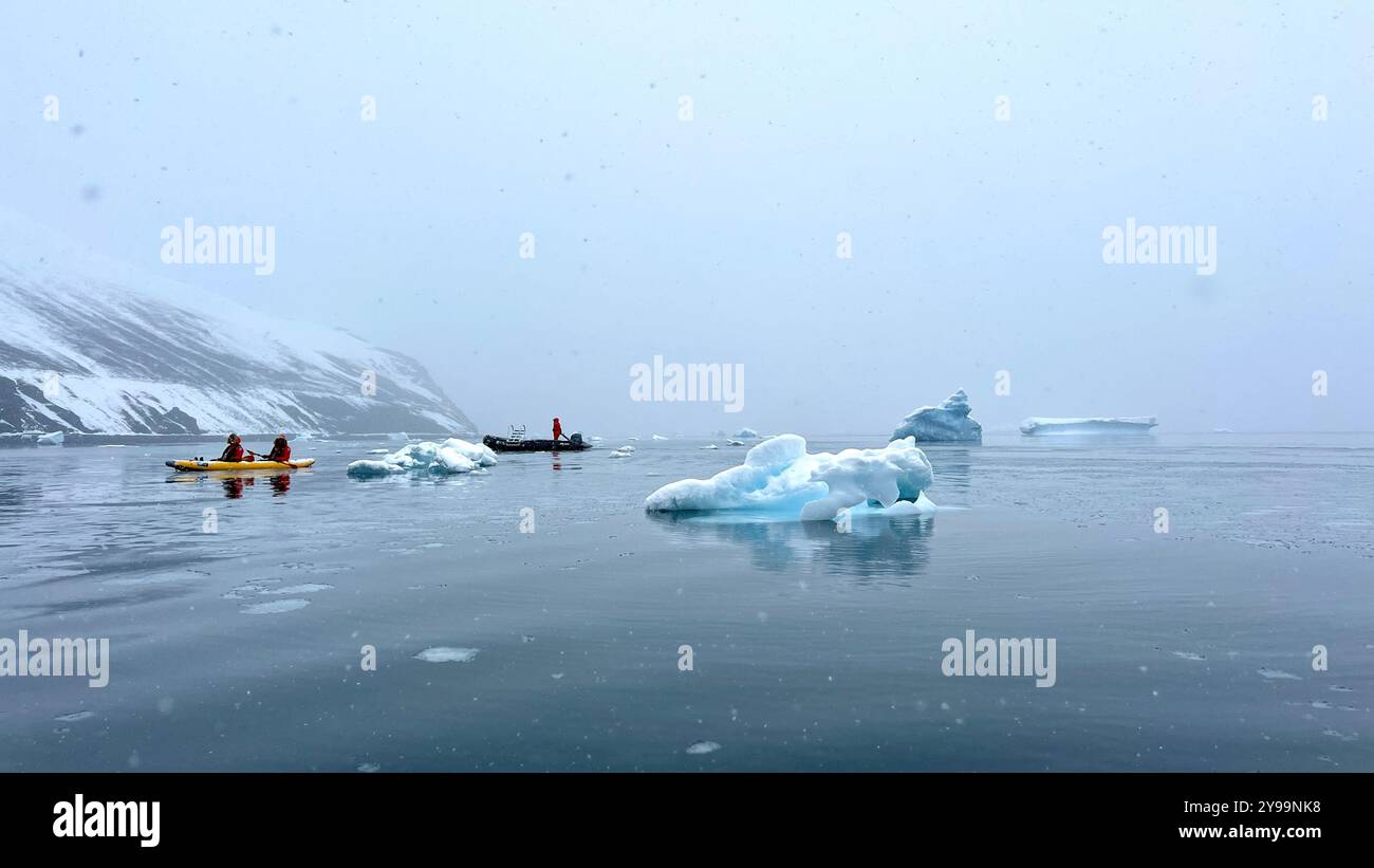 I passeggeri del Nat Geo Endurance kayak da iceberg galleggianti e acque calme vicino alla penisola di Trinity, Antartide, circondati da vette innevate - Immagine stock catturata con smartphone