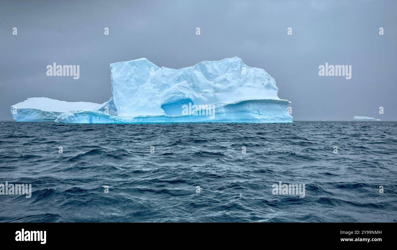 Un enorme iceberg dalle sorprendenti tonalità blu galleggia nelle acque instabili dell'Oceano meridionale, in Antartide - Immagine stock catturata con smartphone