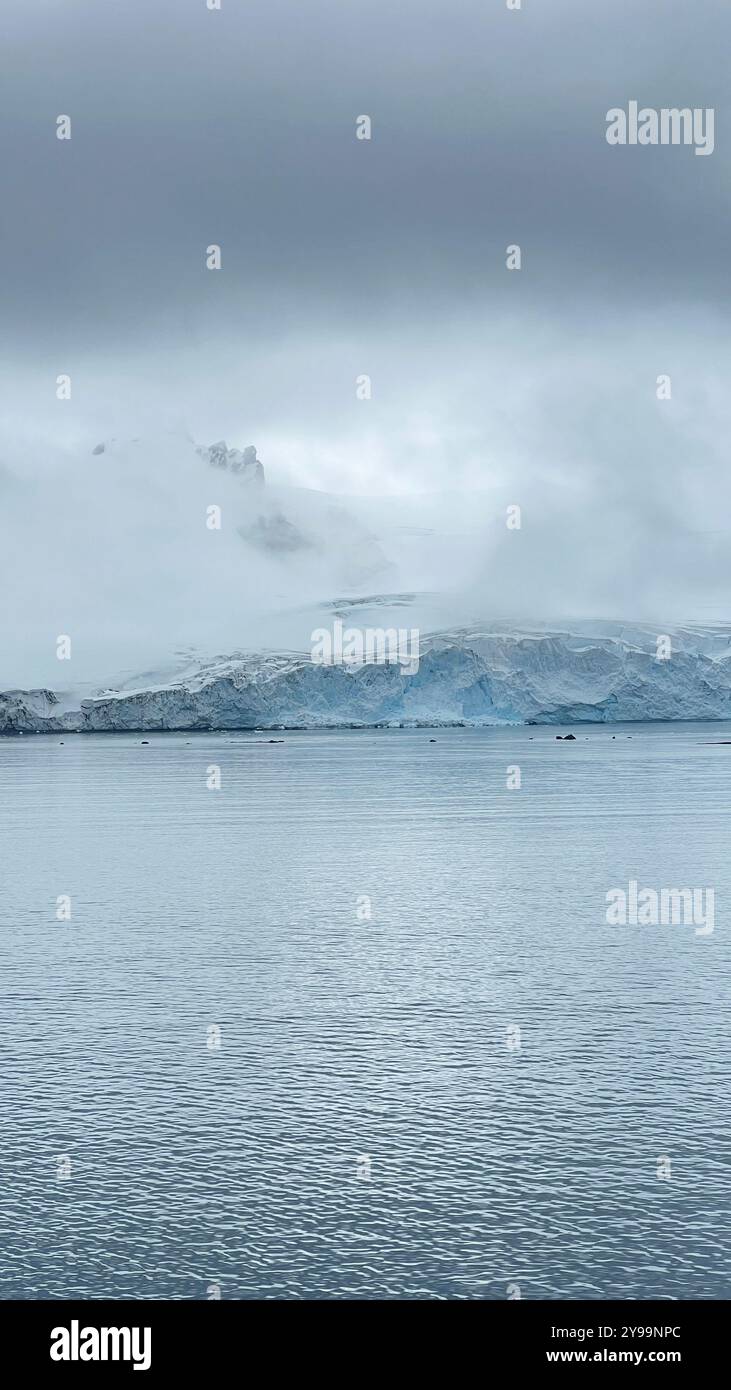 Una tranquilla scena dell'Oceano meridionale in Antartide, con torreggianti cime innevate e ghiacciai che si riflettono nelle acque calme - Immagine stock catturata con smartphone