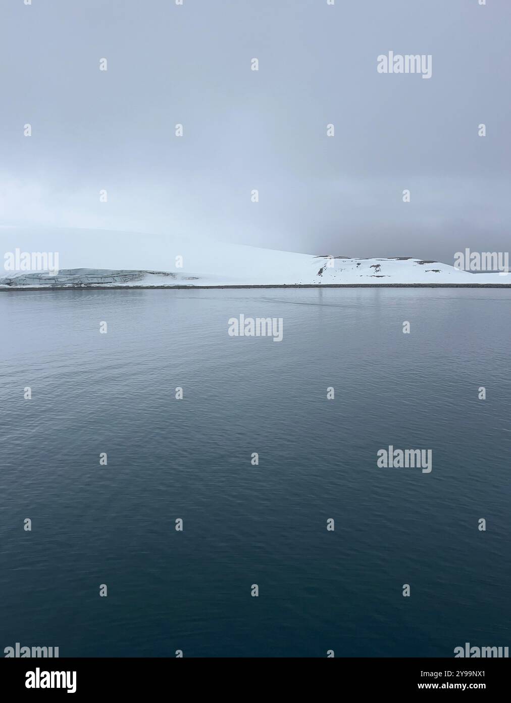 Una vista serena dell'Oceano meridionale in Antartide, con acque lisce che riflettono il cielo coperto e il paesaggio innevato - Immagine stock catturata con smartphone