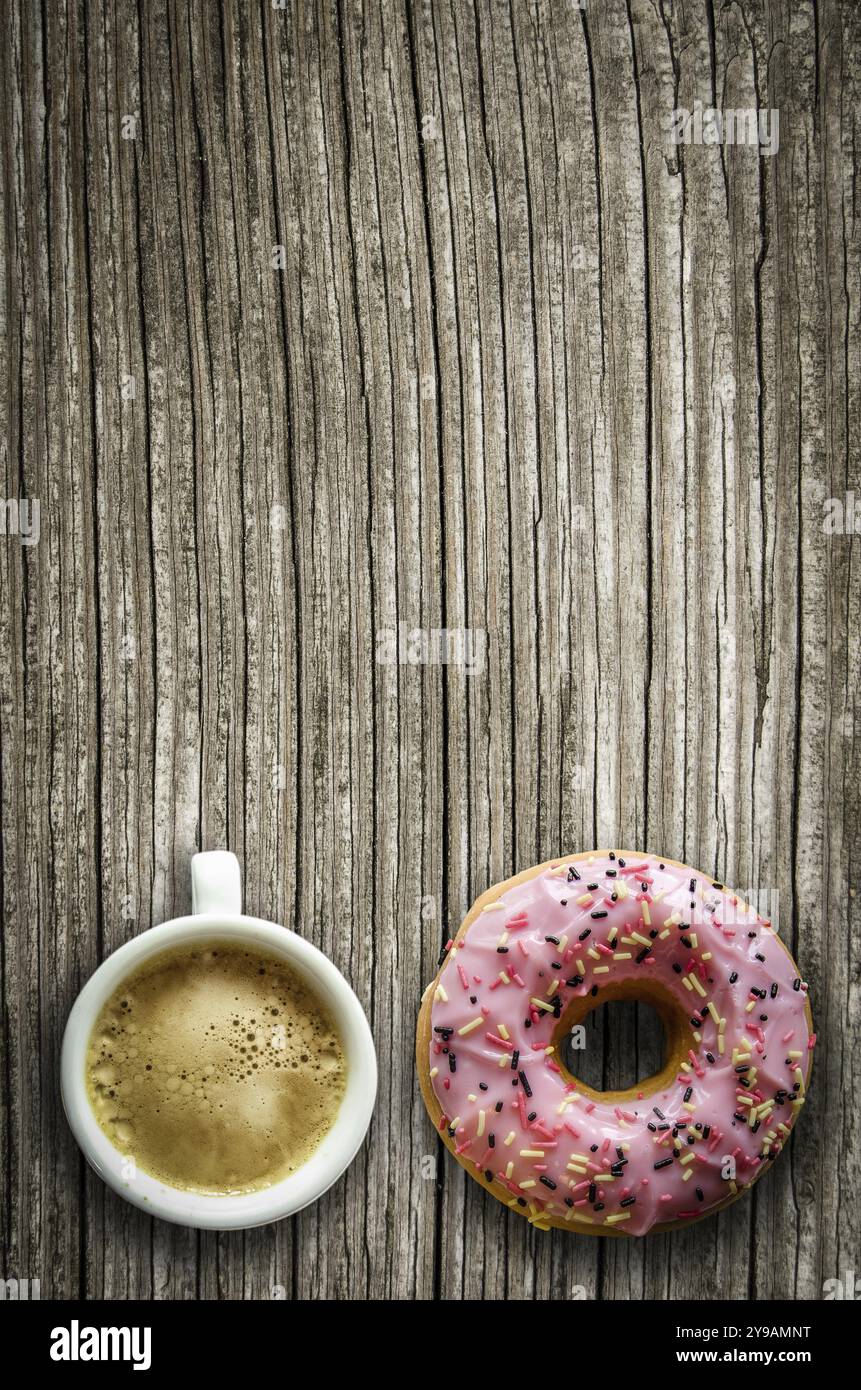 Retrò immagine filtrata di una ciambella di rosa e una tazza di caffè su una tavola in legno rustico con spazio di copia Foto Stock