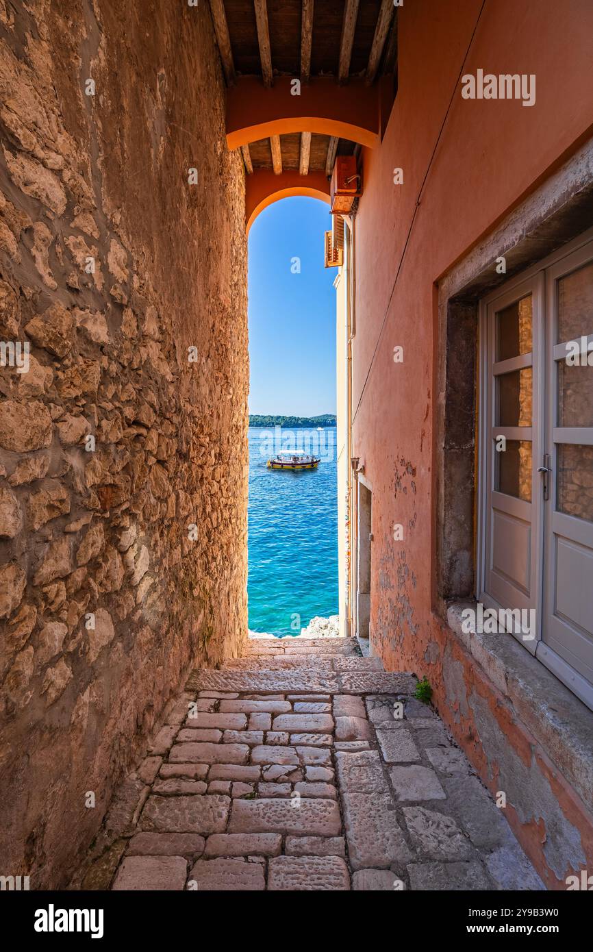 Rovigno, Croazia - tradizionale vicolo acciottolato croato che conduce al mare con barca turistica e cielo azzurro e acqua blu del mare Adriatico Foto Stock