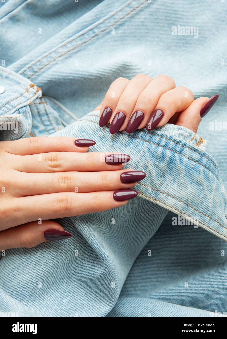 Due mani con splendide unghie Bordeaux delicatamente poste su una giacca casual in denim. L'ambiente mette in risalto uno stile elegante e alla moda con un'atmosfera rilassata Foto Stock