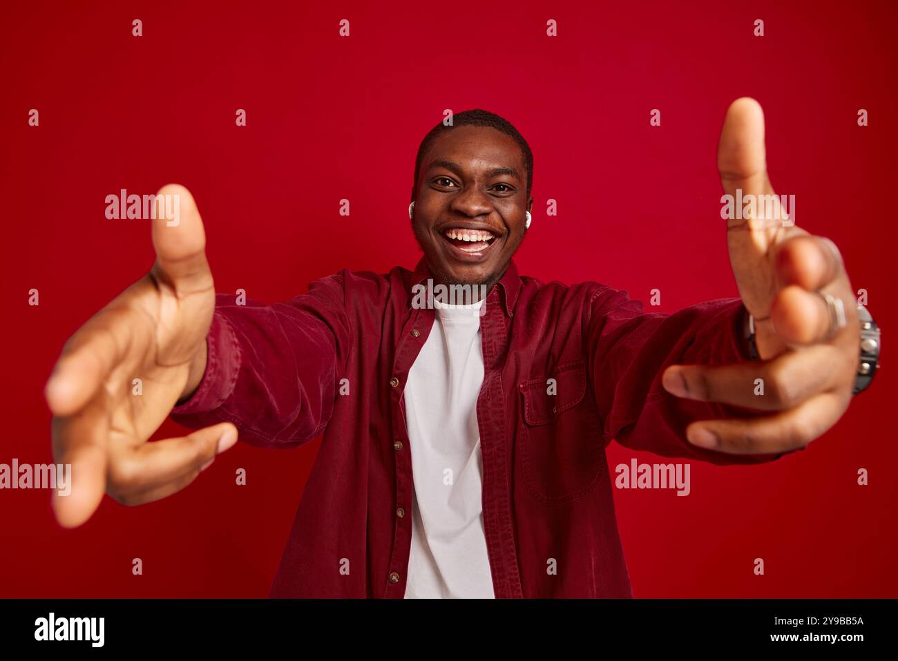 ritratto di un uomo afroamericano emotivo che si rallegra con le mani allungate alla macchina fotografica isolata su sfondo rosso, ritratto in studio Foto Stock