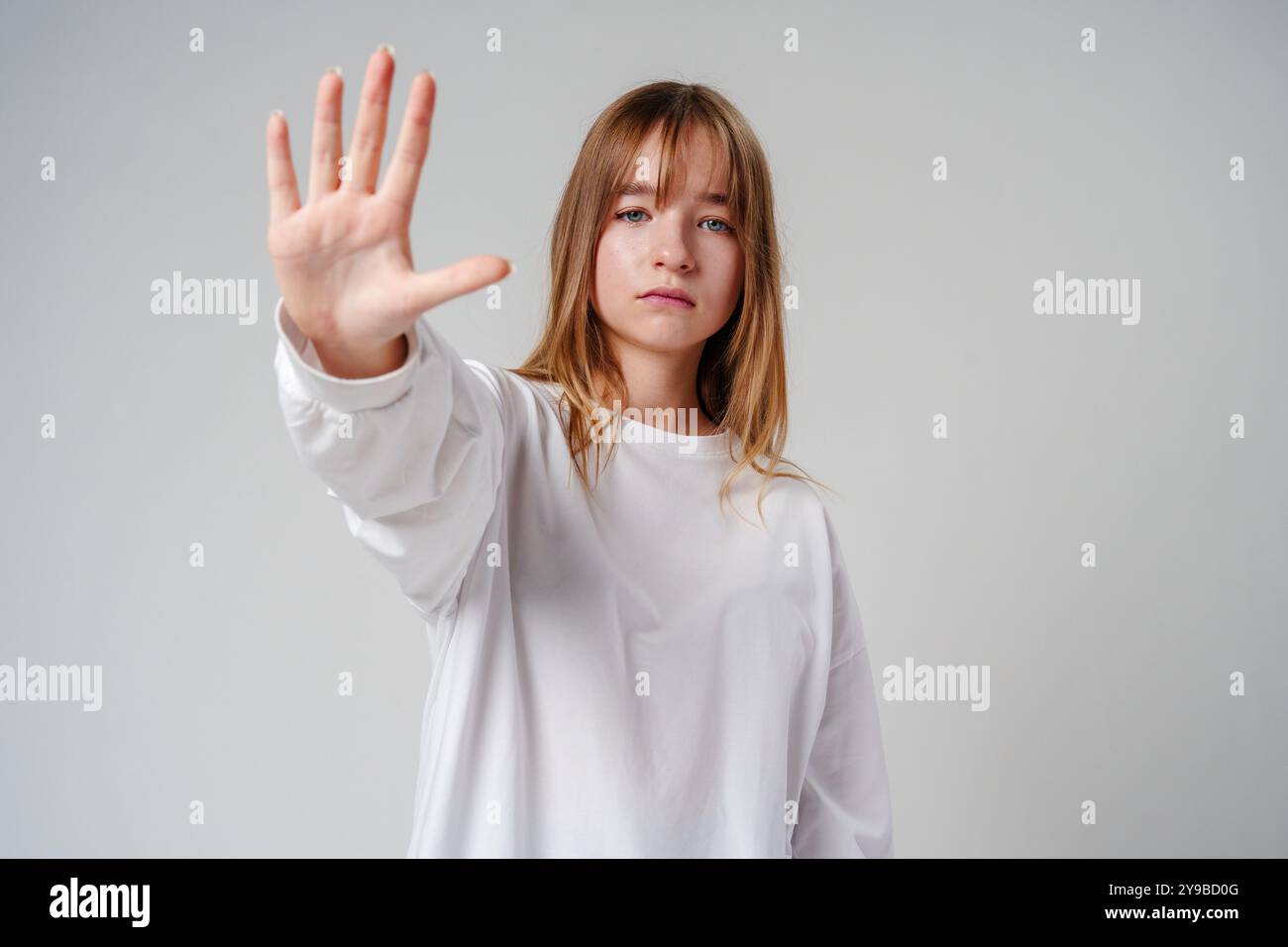 Giovane donna dai capelli lunghi che tiene la mano su uno sfondo semplice Foto Stock