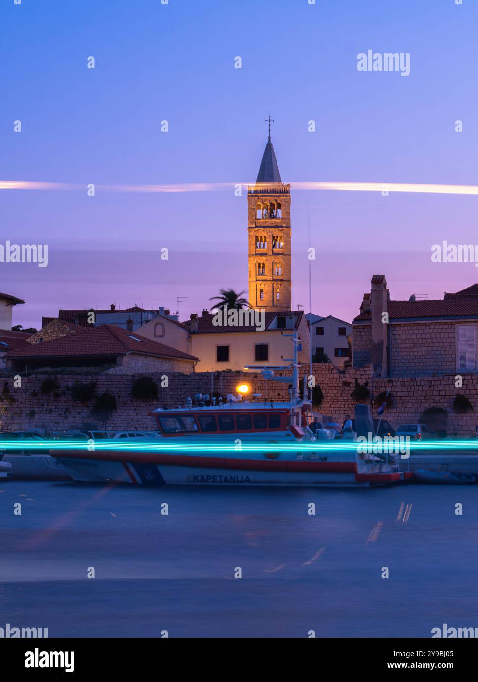 Rab, Croazia - 19 agosto 2023: Una tranquilla città costiera di Rab in Croazia al crepuscolo con un campanile, lungomare, barca della guardia costiera davanti, AN Foto Stock