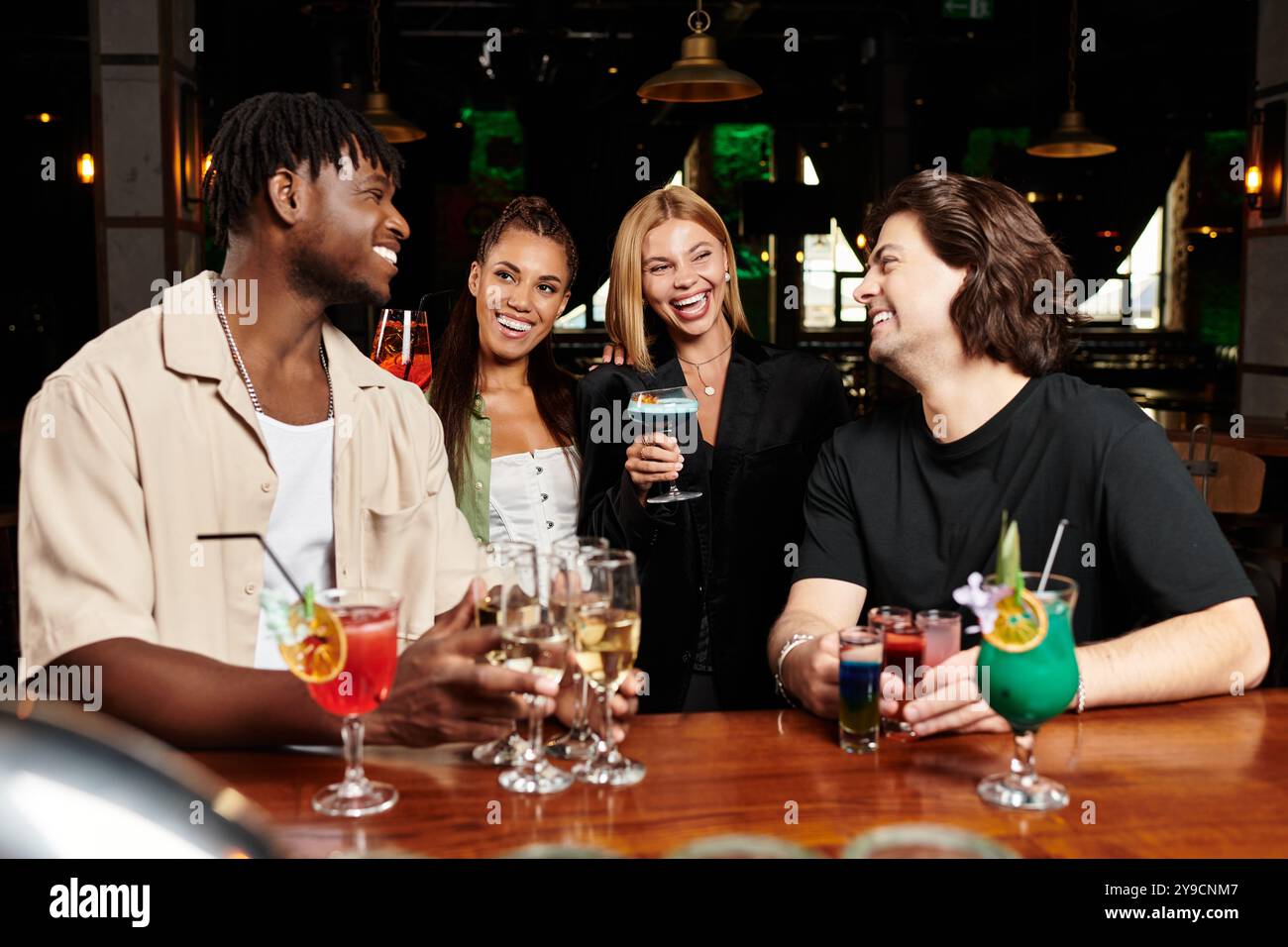 I colleghi brindano con cocktail colorati mentre si scambiano vivaci battute a un divertente raduno. Foto Stock