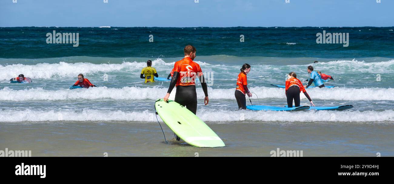 Un'immagine panoramica di un gruppo di principianti di surf che hanno una lezione di surf con istruttori del NQY Activity Centre presso Towan Beach a Newquay. Foto Stock
