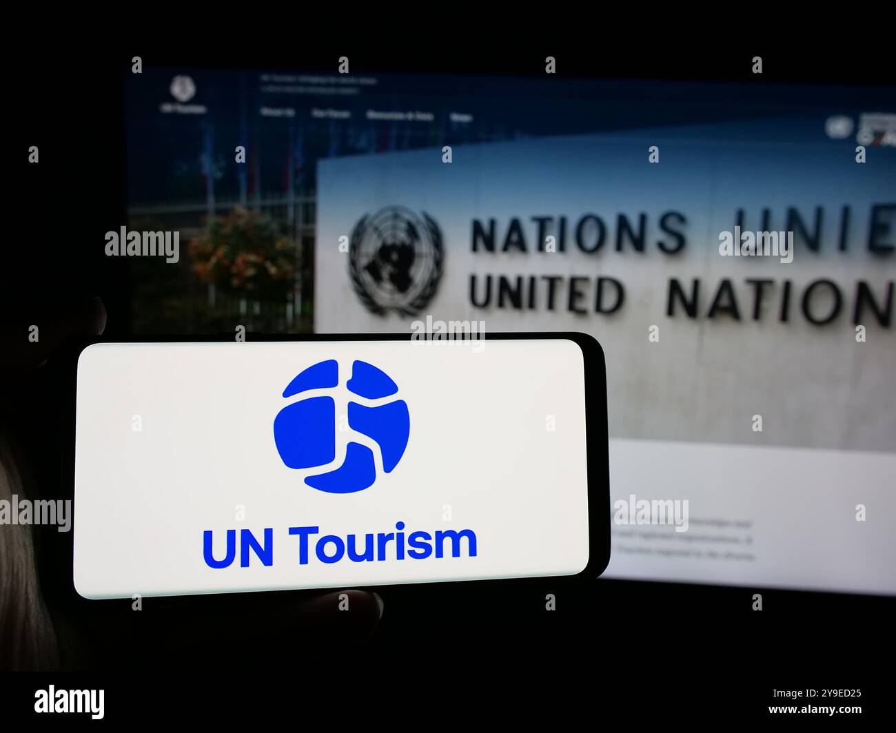 Persona che possiede uno smartphone con il logo dell'agenzia delle Nazioni Unite per il turismo delle Nazioni Unite sullo schermo di fronte al sito web. Mettere a fuoco il display del telefono. Foto Stock