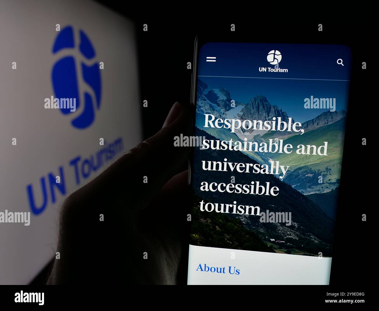 Persona che possiede uno smartphone con la pagina web dell'agenzia delle Nazioni Unite per il turismo delle Nazioni Unite sullo schermo davanti al logo. Messa a fuoco al centro del display del telefono. Foto Stock