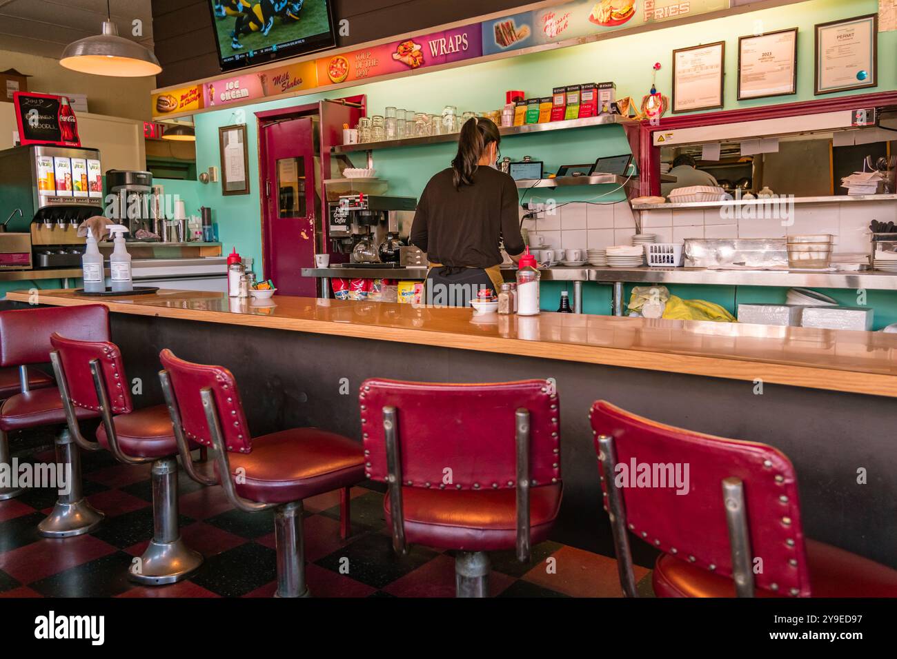 Vancouver, BC, Canada - 15 settembre 2023: Donna lavora dietro il bancone del classico ristorante americano con sedie rosse al bancone. Foto Stock