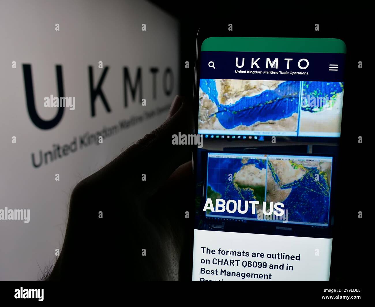 Persona che detiene un telefono cellulare con sullo schermo il sito web di United Kingdom Maritime Trade Operations (UKMTO). Messa a fuoco al centro del display del telefono. Foto Stock