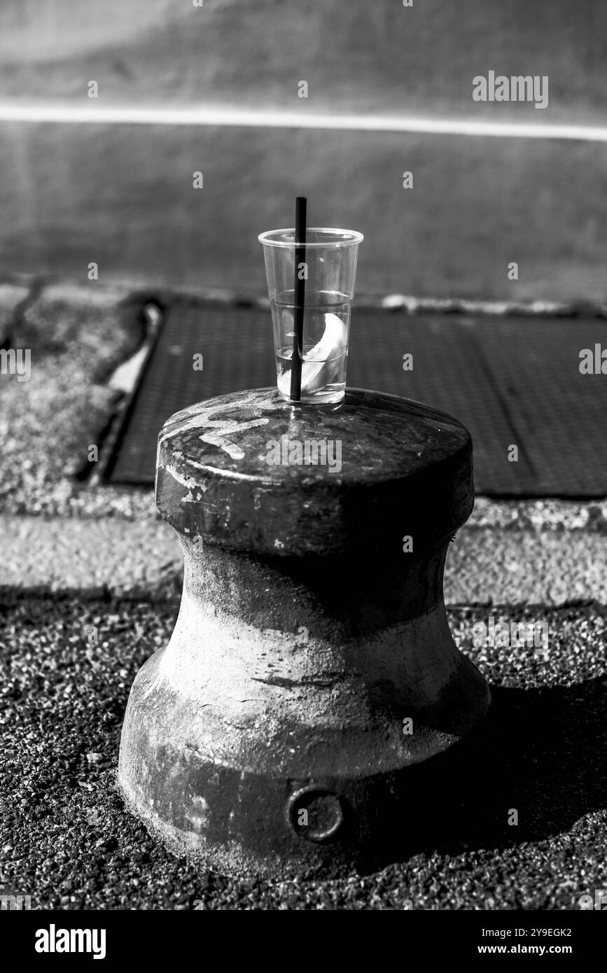 Tazza di plastica abbandonata con paglia nera in cima a un dissuasore stradale con una fetta di arancia e uno Spritz in una strada italiana a Ferrara Foto Stock