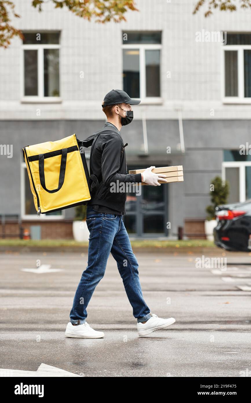 Un addetto alle consegne vestito di nero entra in un edificio per uffici mentre trasporta gli ordini di cibo durante il giorno. Foto Stock