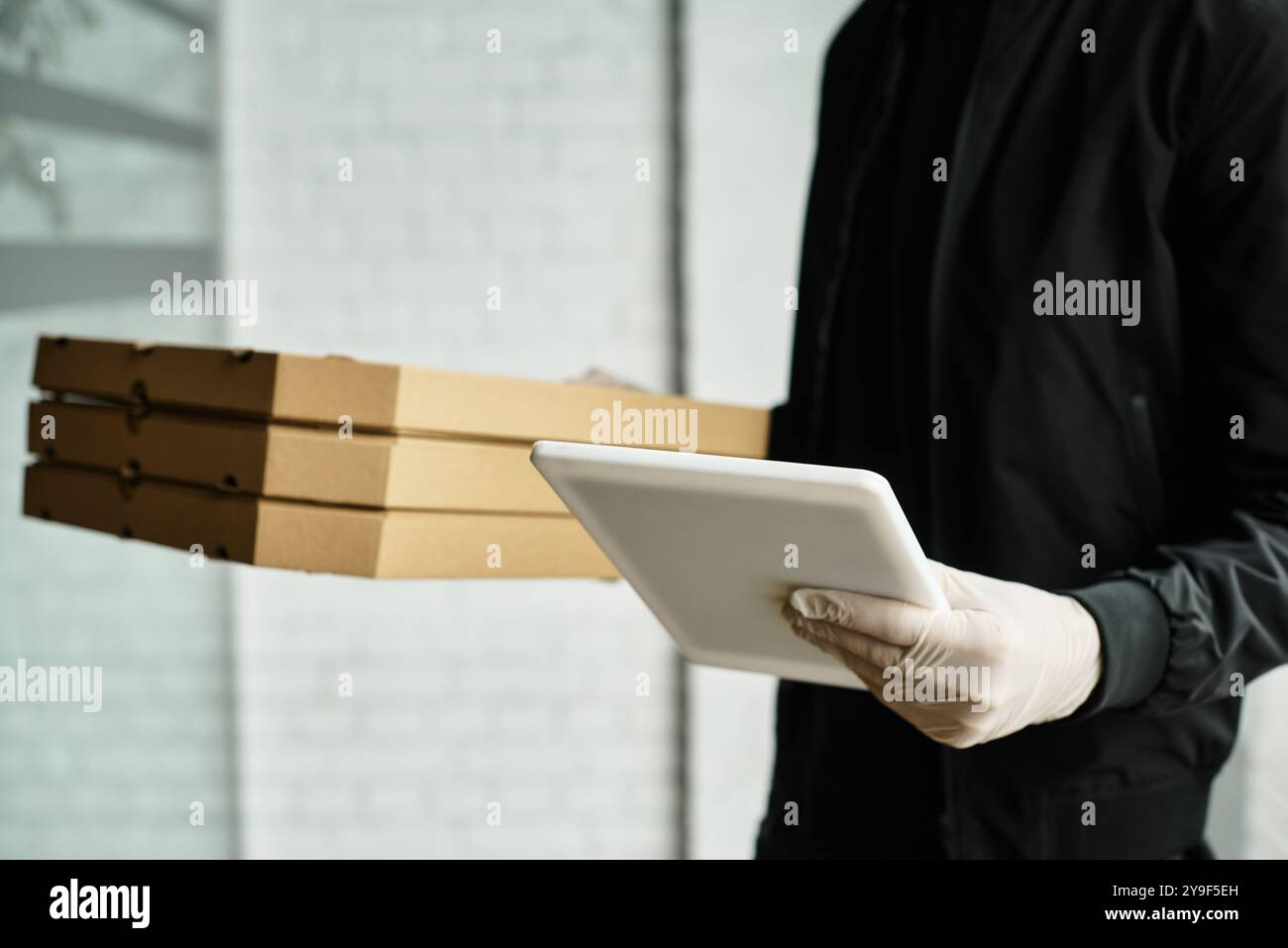 Un addetto alle consegne che indossa guanti porta i pacchi in un edificio per uffici, garantendo la sicurezza. Foto Stock